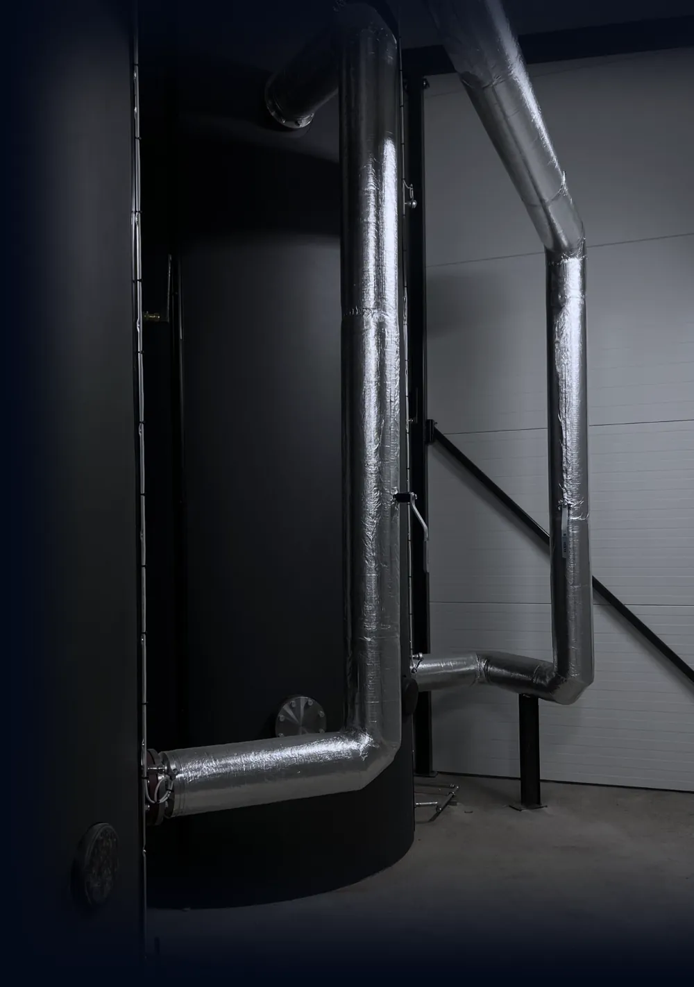 Two black accumulator tanks with insulated pipes in a boiler room