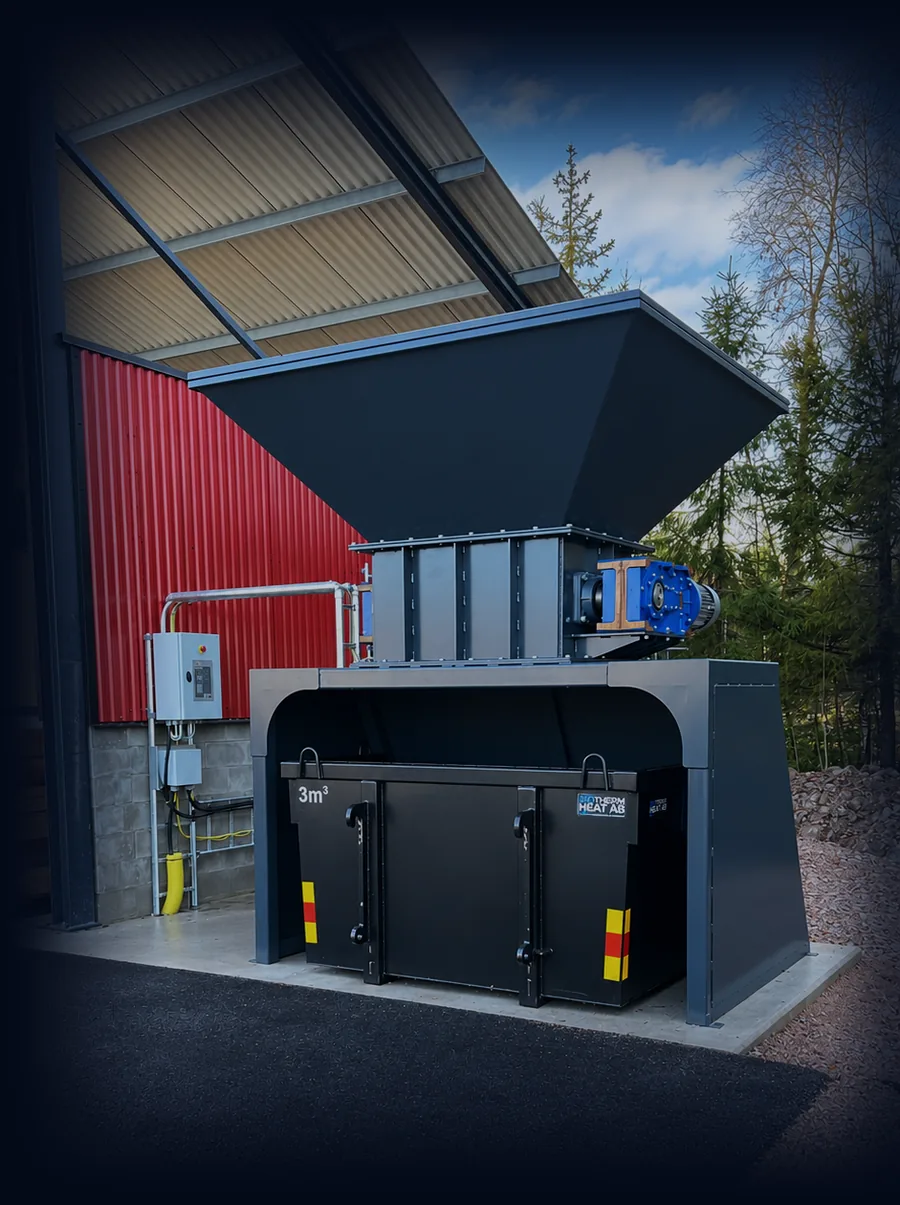 The Shredder installed under a roof in front of a red wall; the 3 m³ bin stands beneath it