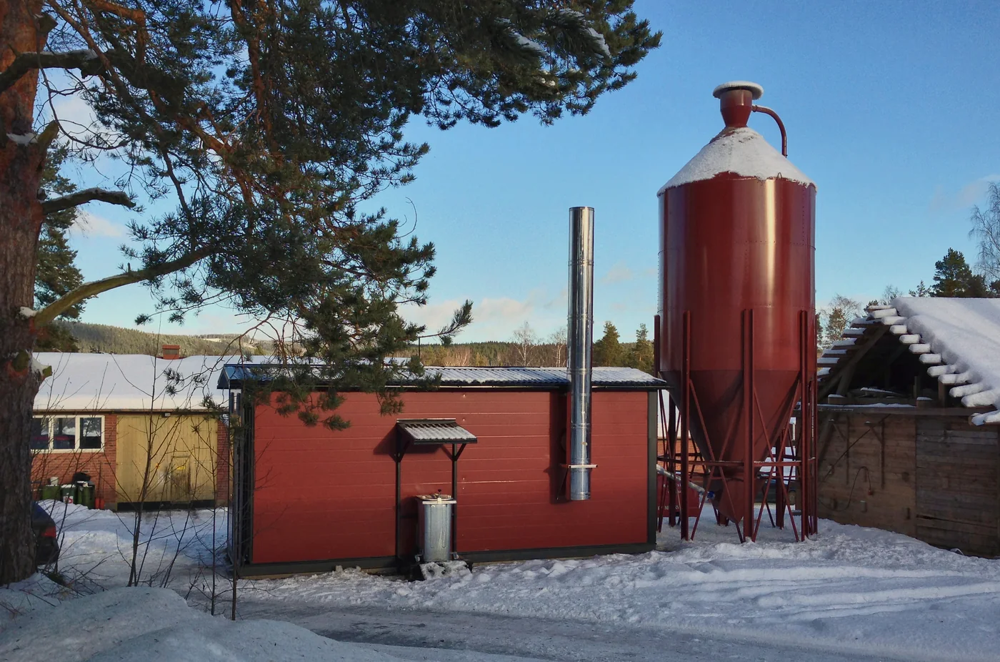 Red boiler house with a pellet silo, chimney and ash container in snow