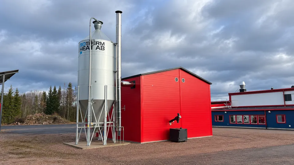 The heating plant with the galvanised pellet silo and the ash container by the wall.