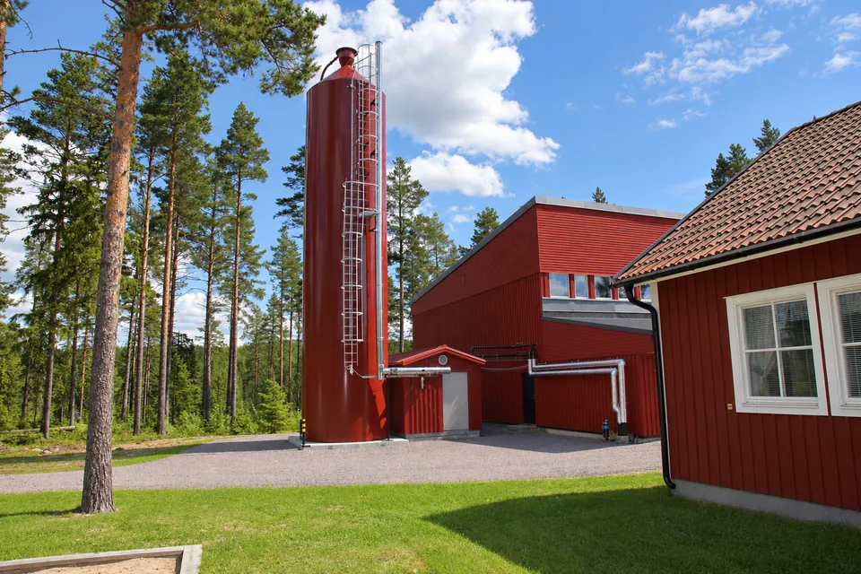 The tall pellet silo among the pines, next to the buildings.